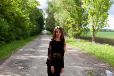 Beautiful slender Ukrainian woman in stylish black clothes on the asphalt old roadの写真素材
