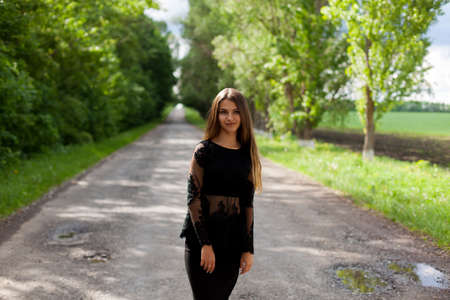 Beautiful slender Ukrainian woman in stylish black clothes on the asphalt old roadの写真素材