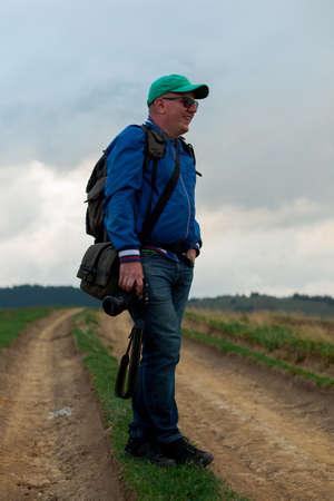 sporty young man in a  cap and jeans with a camera in his hands stands on a footpath high in the mountainsの写真素材