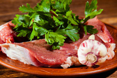 fresh juicy raw steak with cilantro and garlic on a plate and wood backgroundの写真素材