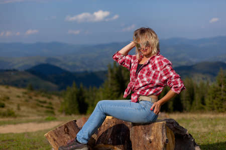 girl in a plaid men's shirt sits on wooden logs high in the carpathian mountainsの写真素材