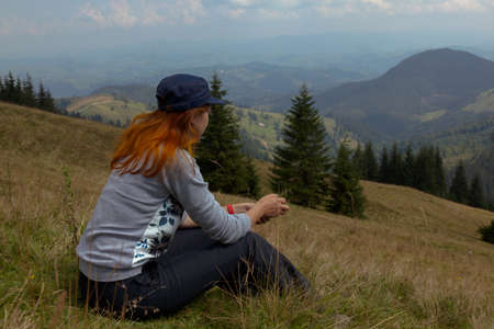on a bright sunny summer day girl sits on the grass in the carpathian mountainsの写真素材