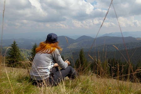 on a bright sunny summer day girl sits on the grass in the carpathian mountainsの写真素材