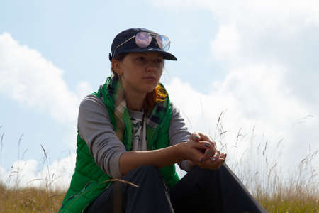 girl sitting on green grass against the background of clouds skyの写真素材