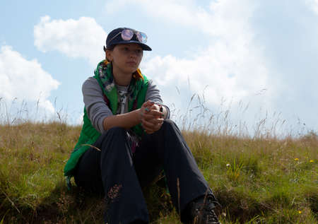 girl sitting on green grass against the background of clouds skyの写真素材