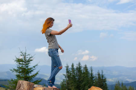 girl takes a selfie on a smartphone in the carpathians on a cloudy sunny summer dayの写真素材