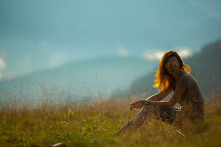 on a bright sunny summer day girl sits on the grass in the carpathian mountainsの写真素材