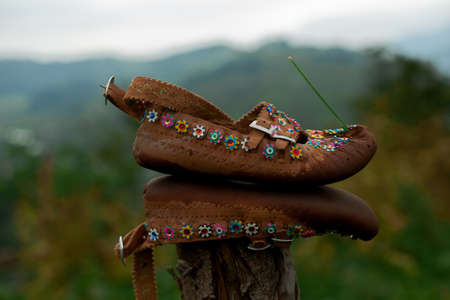 Authentic national Hutsul shoes stand on the fence against the backdrop of the Carpathian mountains