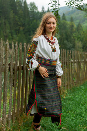 girl in embroidery with a bouquet of wild flowers stands on green grass in the carpathian mountainsの写真素材