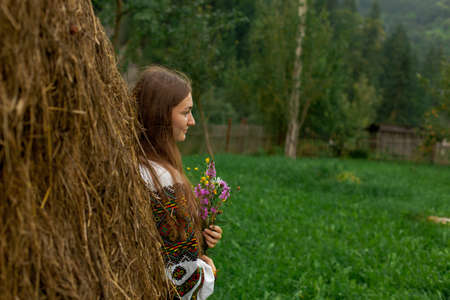 girl in embroidery with a bouquet of wild flowers stands on green grass in the carpathian mountainsの写真素材