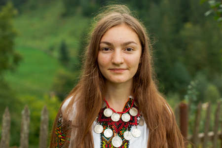 girl in embroidery with a bouquet of wild flowers stands on green grass in the carpathian mountainsの写真素材