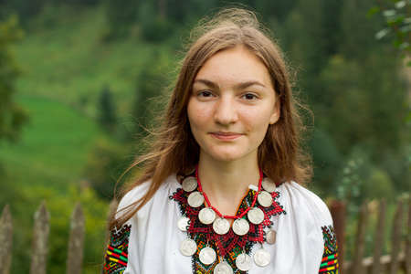 girl in embroidery with a bouquet of wild flowers stands on green grass in the carpathian mountainsの写真素材