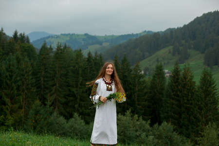 girl in embroidery with a bouquet of wild flowers stands on green grass in the carpathian mountainsの写真素材