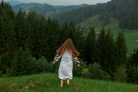 girl with a ripe apple in embroidery sits on green grass under an apple treeの写真素材