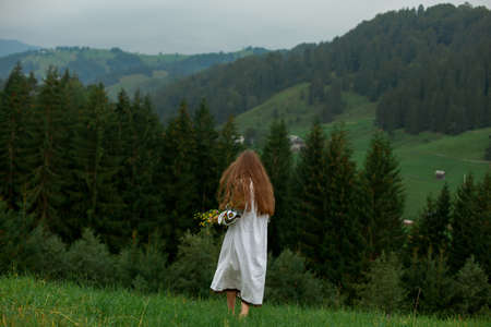 girl in embroidery with a bouquet of wild flowers stands on green grass in the carpathian mountainsの写真素材