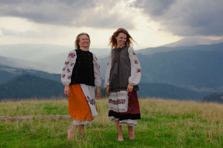 two emotional cheerful girl in Ukrainian embroidery clothes high in the carpathian mountains in summerの写真素材