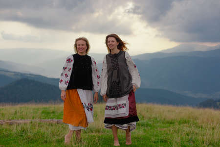two emotional cheerful girl in Ukrainian embroidery clothes high in the carpathian mountains in summerの写真素材