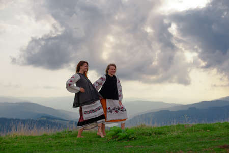 two emotional cheerful girl in Ukrainian embroidery clothes high in the carpathian mountains in summerの写真素材