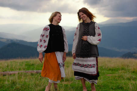 two emotional cheerful girl in Ukrainian embroidery clothes high in the carpathian mountains in summerの写真素材