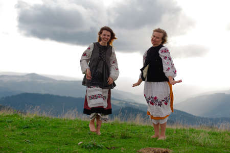 two emotional cheerful girl in Ukrainian embroidery clothes high in the carpathian mountains in summerの写真素材