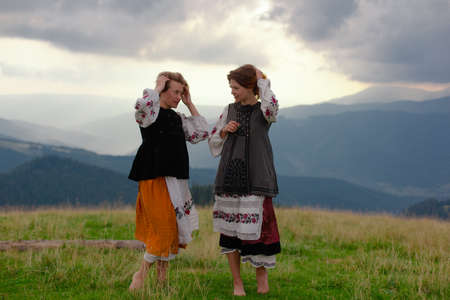 two emotional cheerful girl in Ukrainian embroidery clothes high in the carpathian mountains in summerの写真素材