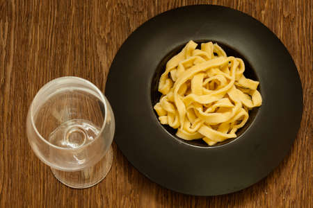 italian pasta served on a black plate with a glass of wineの写真素材
