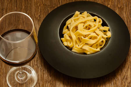 italian pasta served on a black plate with a glass of wineの写真素材
