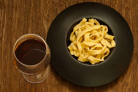 italian pasta served on a black plate with a glass of wineの写真素材
