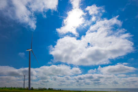 against the background of a blue sky with white clouds, a green electricity wind turbine generator on the seashoreの写真素材