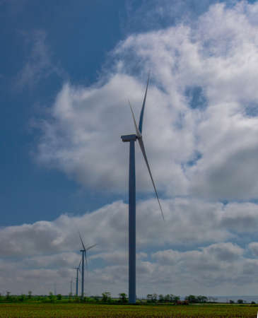 against the background of a blue sky with white clouds, a green electricity wind turbine generator on the seashoreの写真素材