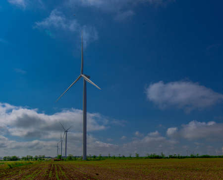 Under the blue sky with white clouds, the propeller of the green electricity generator is mounted on the side of the road in the fieldの写真素材