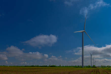 Under the blue sky with white clouds, the propeller of the green electricity generator is mounted on...