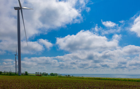 against the background of a blue sky with white clouds, a green electricity wind turbine generator on the seashoreの写真素材