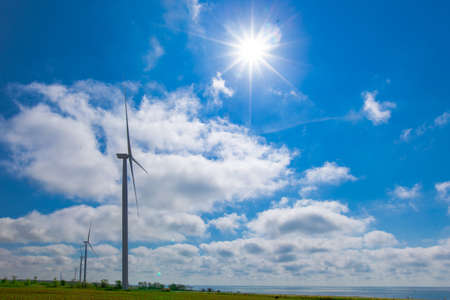 against the background of a blue sky with white clouds, a green electricity wind turbine generator on the seashoreの写真素材