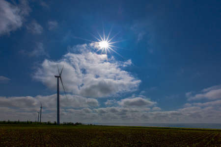 against the background of a blue sky with white clouds, a green electricity wind turbine generator on the seashoreの写真素材