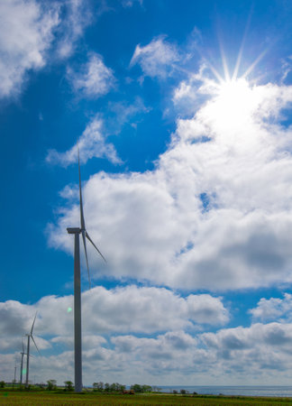 against the background of a blue sky with white clouds, a green electricity wind turbine generator on the seashoreの写真素材