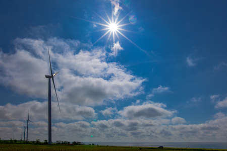 against the background of a blue sky with white clouds, a green electricity wind turbine generator on the seashoreの写真素材