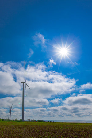 against the background of a blue sky with white clouds, a green electricity wind turbine generator on the seashoreの写真素材