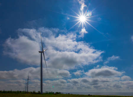 against the background of a blue sky with white clouds, a green electricity wind turbine generator on the seashoreの写真素材