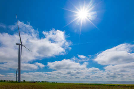 against the background of a blue sky with white clouds, a green electricity wind turbine generator on the seashoreの写真素材