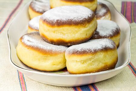 Group of fresh donuts sprinkled with powdered sugar in plate, on old ukrainian linen tableclothの写真素材
