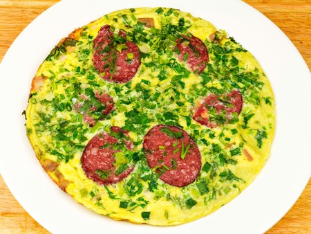 Omelette with sausage and herbs in white plate on wooden table, top view.の写真素材