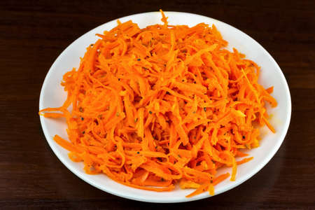 Spicy salad of grated carrots and parsley in plate, on wooden background, top viewの写真素材