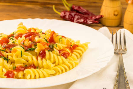 Italian pasta fusilli with tomato sauce in plate, napkin and fork on wooden table.の写真素材