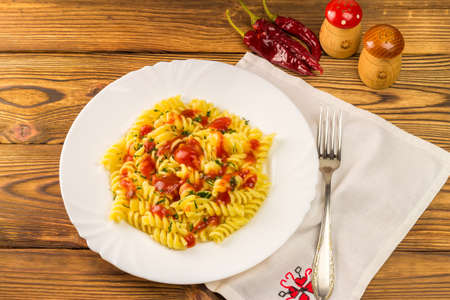 Italian pasta fusilli with tomato sauce in plate, napkin and fork on wooden table.の写真素材