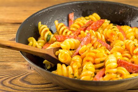 Italian pasta fusilli with tomato sauce and sausage in pan, wooden spoon on table.の写真素材