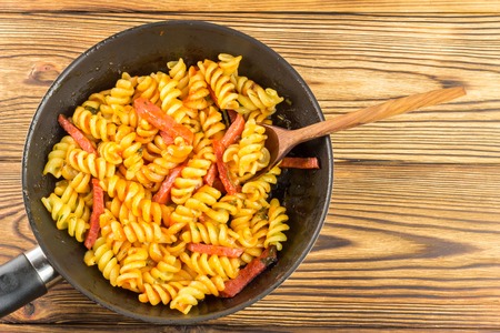 Italian pasta fusilli with tomato sauce and sausage in pan, wooden spoon on table, top view, space for text.の写真素材