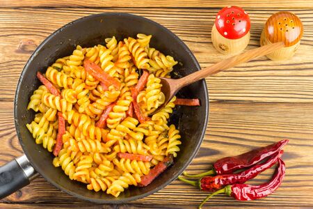 Italian pasta fusilli with tomato sauce and sausage in pan, wooden spoon, red pepper on table, top view, space for text.の写真素材