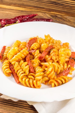 Italian pasta fusilli with tomato sauce and sausage in plate, napkin, pepper on wooden table.の写真素材