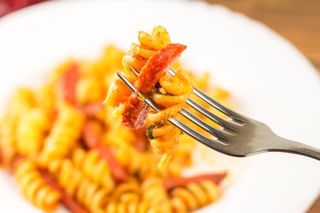 Italian pasta fusilli with tomato sauce and sausage skewered on fork in plate, close-up, selective focus.の写真素材